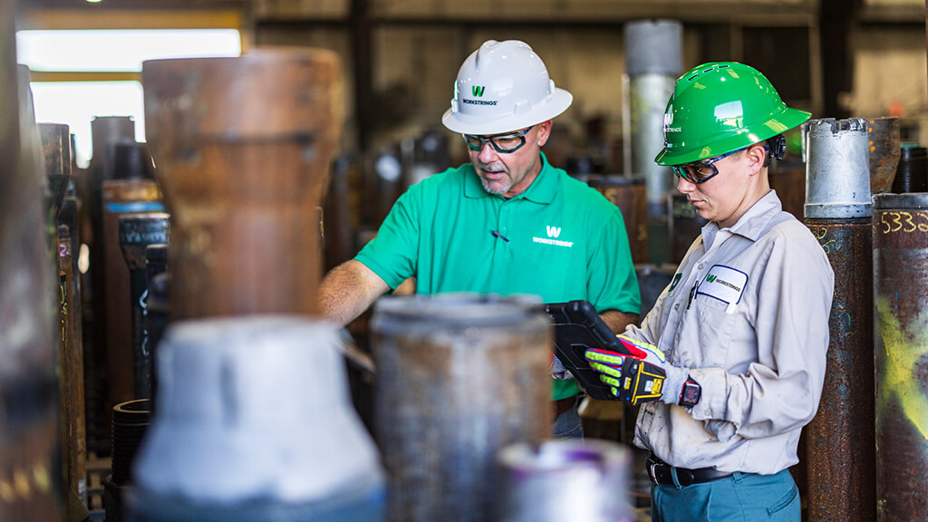 Two Workstrings employees reviewing the quality of drill pipes in a warehouse